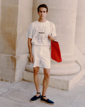 A young man outdoors wears Seersucker Double-Button Shorts and a t-shirt, holding a red bag and sporting black espadrilles.