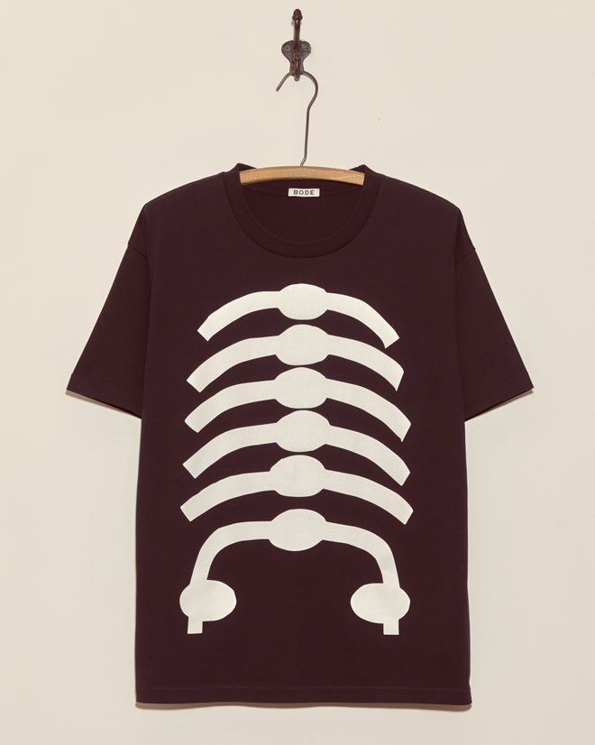 The Skeleton Tee features a black base with a white ribcage graphic on the front, displayed on a wooden hanger—ideal for Halloween or vintage skeleton-inspired looks.