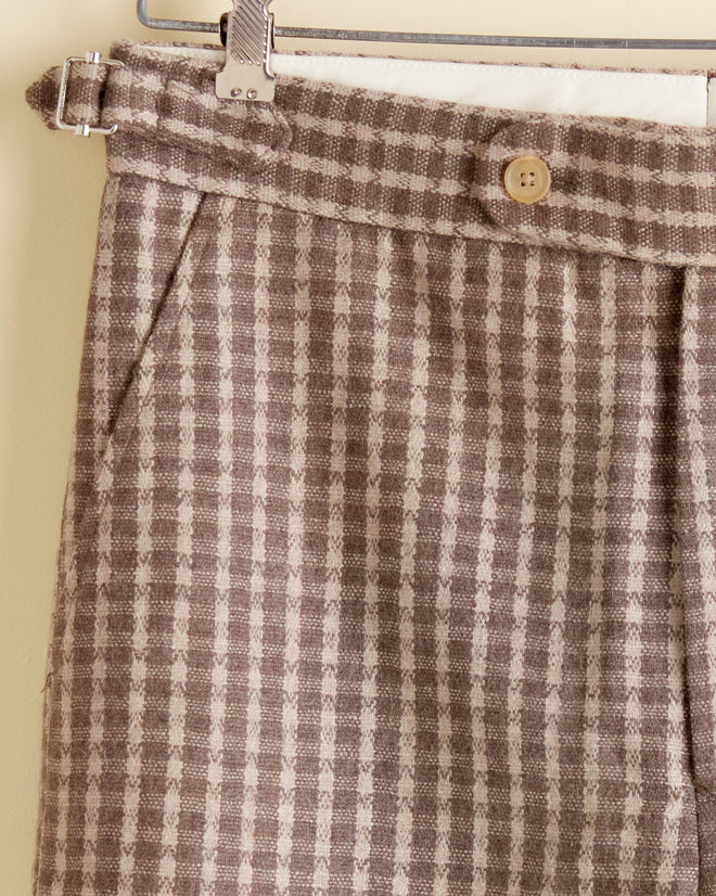 Close-up of the Acorn Check Trousers - 30, unique plaid wool trousers with button and belt loop details, hanging on a metal hanger.