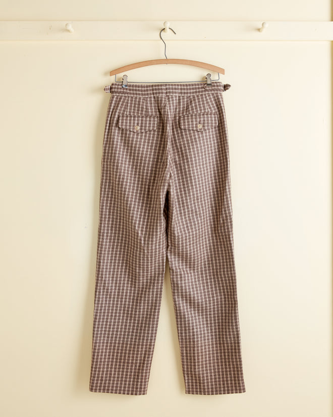 Acorn Check Trousers - 30 in brown and white plaid wool, displayed on a wooden hanger against a cream-colored wall.