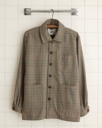 An Airedale Jacket - S/M, uniquely designed in brown plaid made from 100% wool and featuring button closures, is hanging on a white tiled wall.