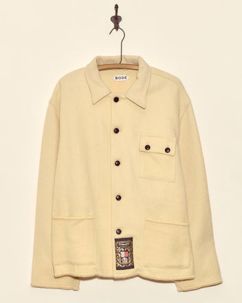 Almond Blanket Jacket - XL/XXL: a cream-colored, midcentury-inspired wool jacket with three front pockets, made in New York. One-of-a-kind piece shown hanging on a hook against a plain background.