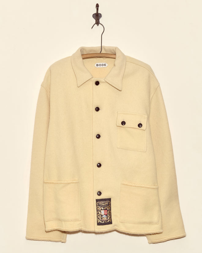 Almond Blanket Jacket - XL/XXL: a cream-colored, midcentury-inspired wool jacket with three front pockets, made in New York. One-of-a-kind piece shown hanging on a hook against a plain background.