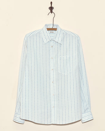 The Alpine Row Shirt - M is a light blue long-sleeve button-up, made from vintage shirting fabric with vertical blue and white dotted stripes, and hangs on a hook.