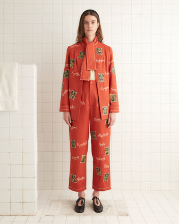 A person wearing an elongated fit, scarlet wool suit and black shoes stands in a tiled room on a white mat, featuring the Alumni Jacket.