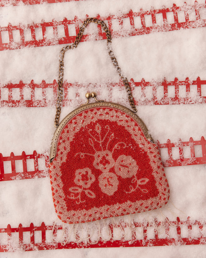 Amrita Beaded Bag, showcasing a vintage red and white floral pattern, elegantly displayed on a snowy surface with a decorative background.