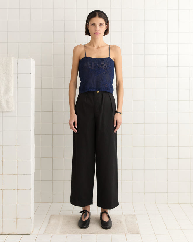 A person wearing the "Angel Fish Tank - Navy" and black pants stands in a tiled room, gazing at the camera.