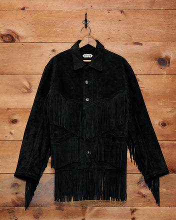 Appalachian Jacket - Black suede jacket featuring hand-cut fringe, shown hanging on a hook against a wooden wall background—perfect for adding a touch of Western flair to any outfit.