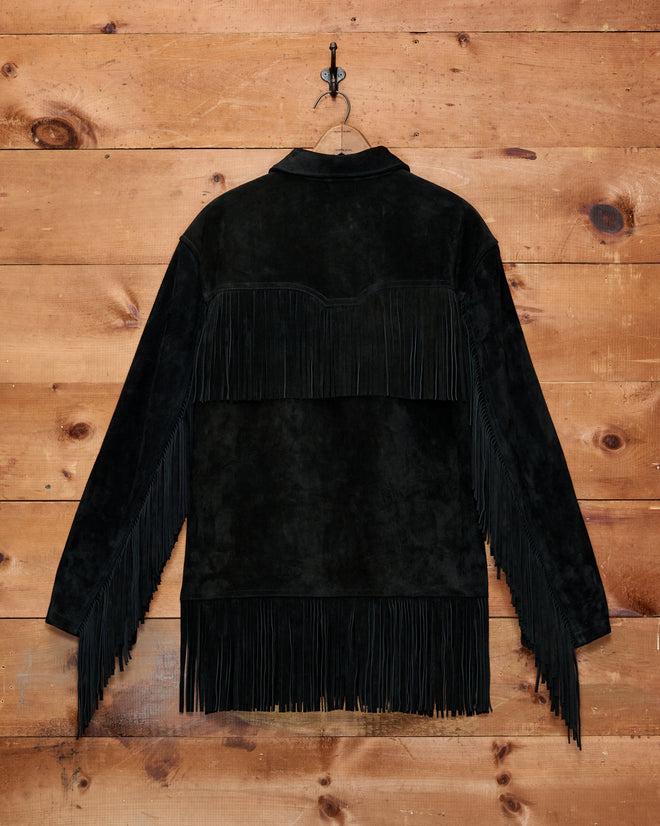 Appalachian Jacket - Black, featuring hand-cut fringe detail on the back and sleeves, hangs on a hook against a wood wall.