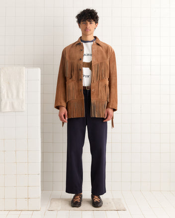 A person stands in a tiled room wearing the Appalachian Jacket - Light Brown, styled with a white shirt, navy pants, and black shoes.