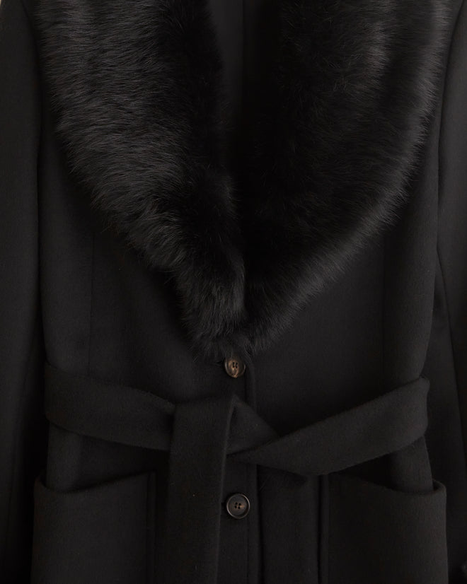 A woman with short hair dons the Arena Coat, featuring a black wool design with a fur collar, looking directly at the camera.