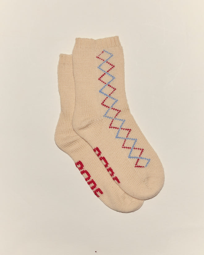 Two beige Argyle Sketch Socks with a red and blue diamond pattern and red text on the sole, displayed on a white background, add cozy Bode-inspired style to any wardrobe.
