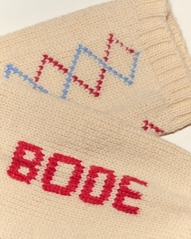 Close-up of beige knit Argyle Sketch Socks from Bode featuring “BOOE” in red and a red and blue diamond pattern, inspired by classic embroidered socks.