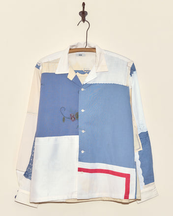The Aster Napkin Shirt - M/L, featuring blue, white, and red patchwork, hangs on a metal hook against a cream wall.