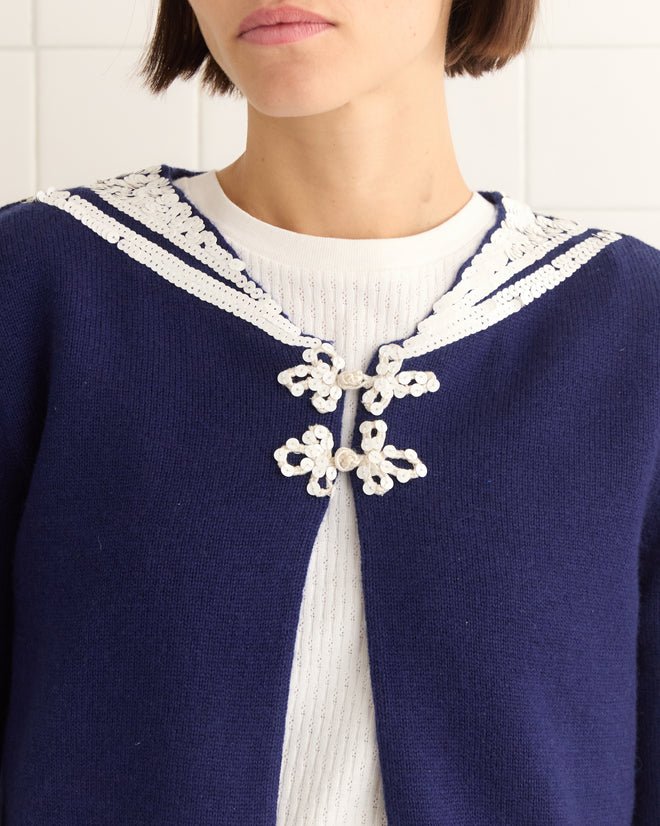 Person wearing the Astoria Cardigan in navy, featuring lace details and a sailor collar, over a white ribbed top.