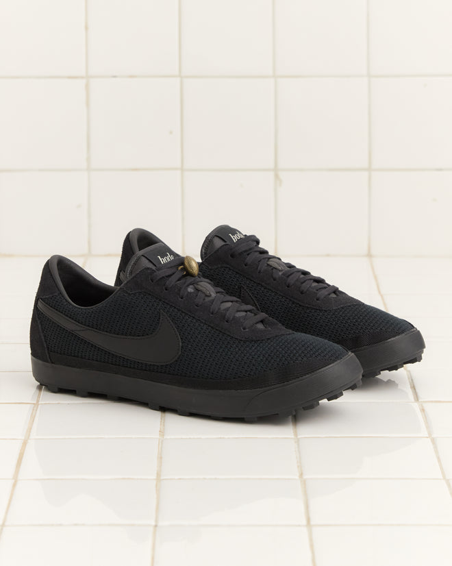 A pair of Bode Rec. and Nike Astrograbber sneakers in black, recognizable by their swoosh logo and waffle sole, rests on a white tiled floor.