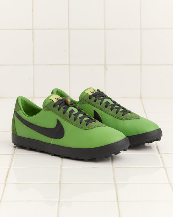 The Bode Rec. and Nike Astrograbber - Green sneakers, featuring a black swoosh, are set against a white tiled background, evoking the innovative spirit of Bill Bowerman.