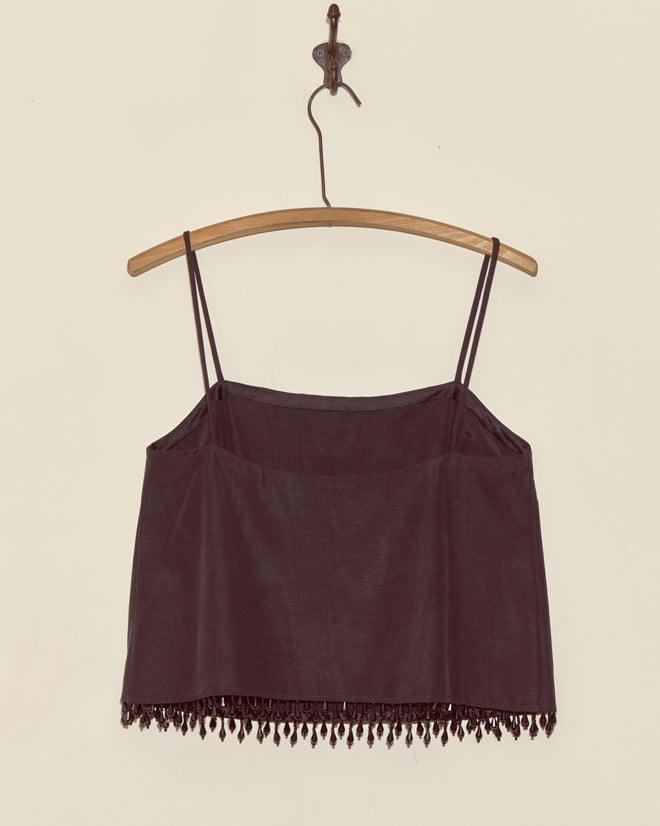 The Anglia Jet Tank - S is a vintage faille crop top with thin straps and droplet bead tassels, displayed on a wooden hanger against a beige wall.