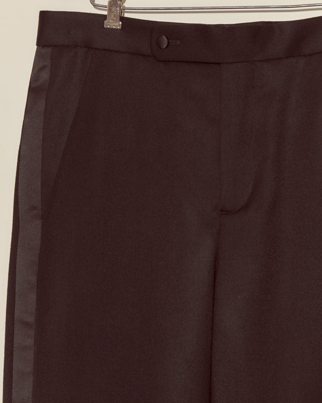 Close-up of Barathea Tuxedo Trousers in black wool hanging on a hanger, showcasing the waistband, button, and side pocket.
