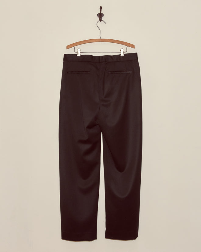 Barathea Tuxedo Trousers in black, 1950s style, displayed on a wooden hanger against a plain beige wall, shown from the back.
