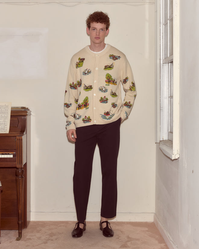A man stands indoors wearing the Beaded Camp Cardigan, which features colorful details, paired with black pants and black shoes.