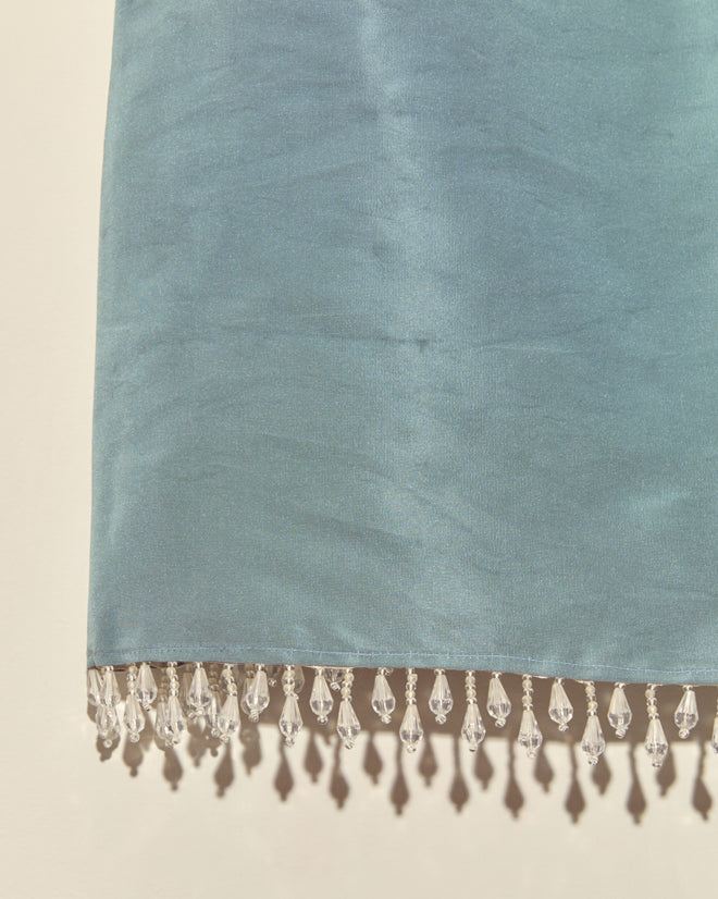 The Beaded Frost Tank - S features light blue silky fabric with clear droplet beads in a teardrop fringe along the bottom edge, inspired by vintage faille tanks and shown against a neutral background.