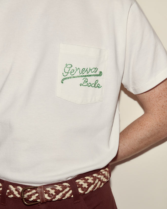Wearing the Beaded Geneva Pocket Tee, featuring "Geneva Lake" on the pocket, with maroon pants and a braided belt—perfect attire for relaxing by Camp Geneva.
