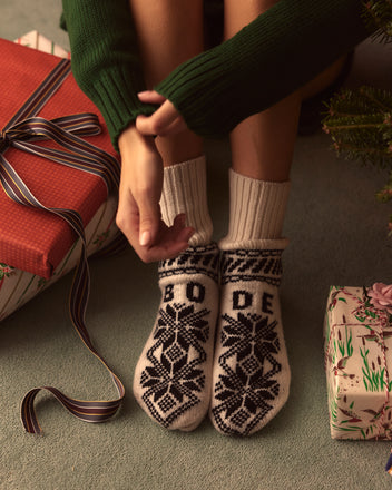 A person in Snowflake Jacquard Socks sits near wrapped gifts on a carpet, surrounded by the warmth of European children's mittens adorned with a charming decorative pattern.