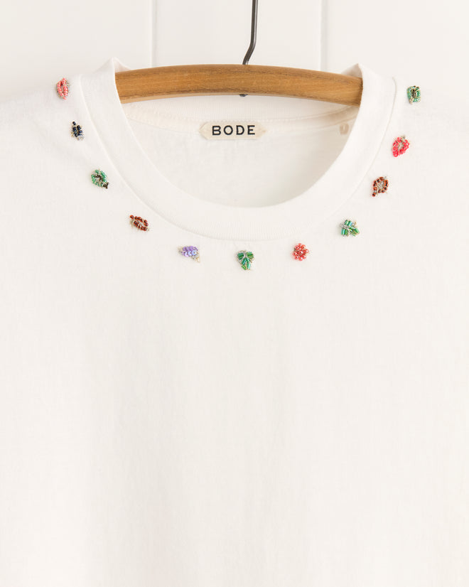 Beaded Necklace Tee on hanger, made from 100% cotton, features small colorful embroidered insects around the neckline—an eye-catching piece inspired by vintage sari appliqués.