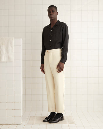 A person wearing a black shirt and Beaded Player Trousers from the 1950s-1960s era stands in a tiled room beside a white towel on a rack.