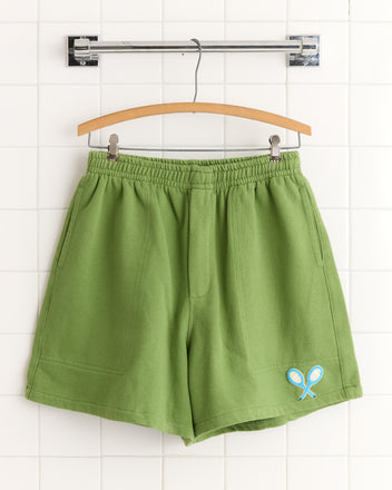 Beaded Racquet Patch Shorts in green with an elastic waistband and a small beaded racquet patch, displayed on a wooden hanger.