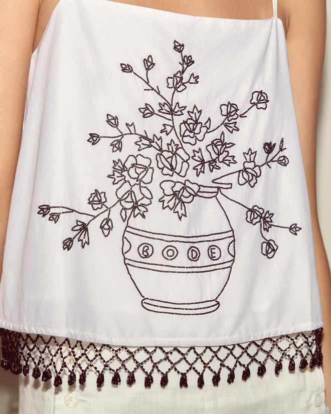 The Beaded Rosebloom Tank is a white cotton poplin tank with black floral embroidery in a vase and an elegant beaded fringe trim at the hem.