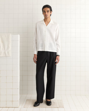 A person in a crisp Belvoir Shirt and black pants stands in a tiled room near a towel.