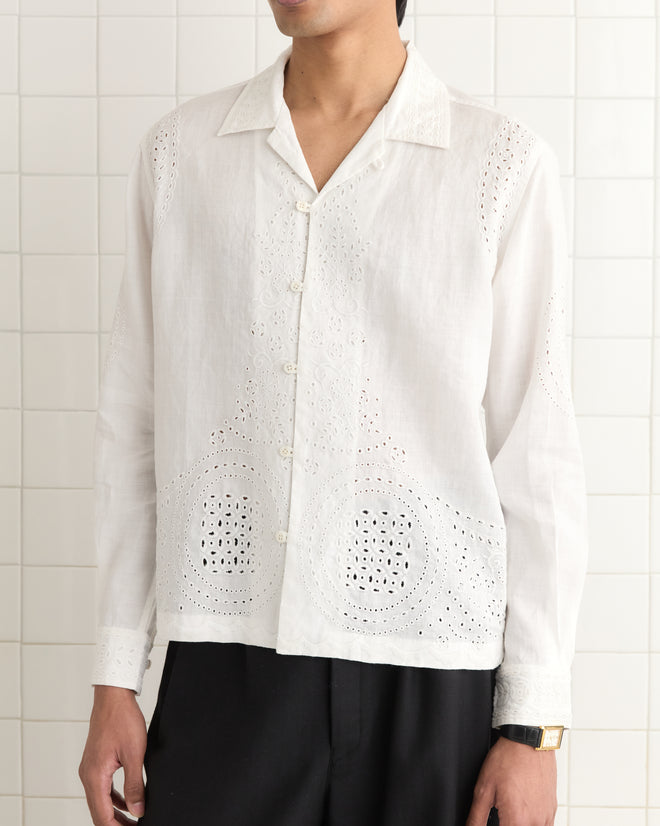 A person wearing the Belvoir Shirt, a white embroidered linen button-up with small geometric patterns, stands against a tiled background.