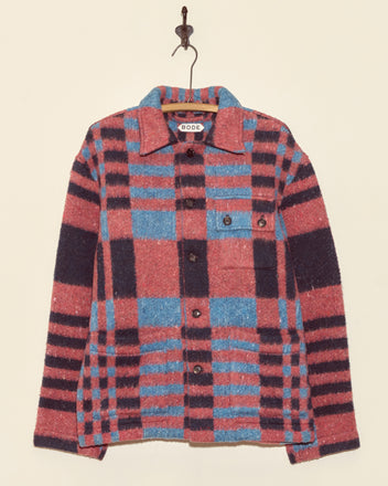 The Berry Crate Jacket - S/M is a unique wool jacket in pink and blue plaid with black accents, displayed hanging on a hook against a plain wall.