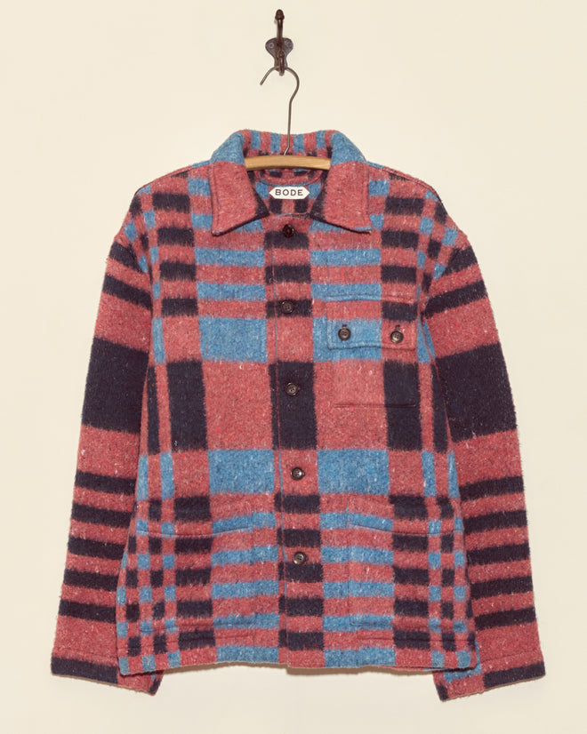 The Berry Crate Jacket - S/M is a unique wool jacket in pink and blue plaid with black accents, displayed hanging on a hook against a plain wall.