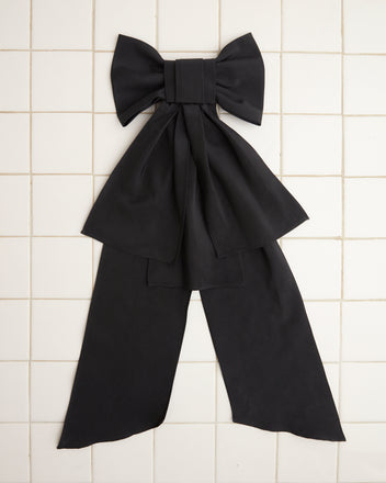 The Bevel Bow, featuring an oversized silhouette of a large, hand-made black design, rests elegantly against a white tiled background.