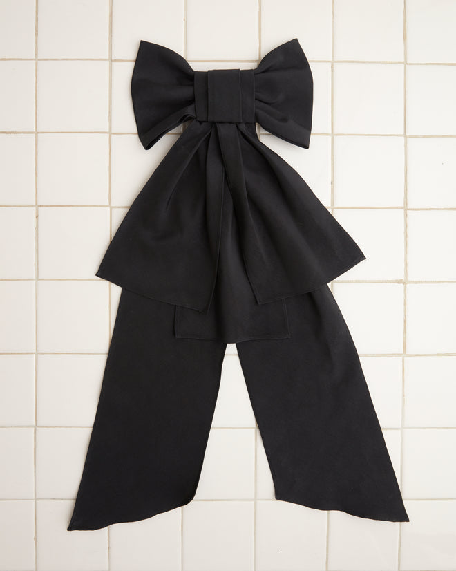 The Bevel Bow, featuring an oversized silhouette of a large, hand-made black design, rests elegantly against a white tiled background.