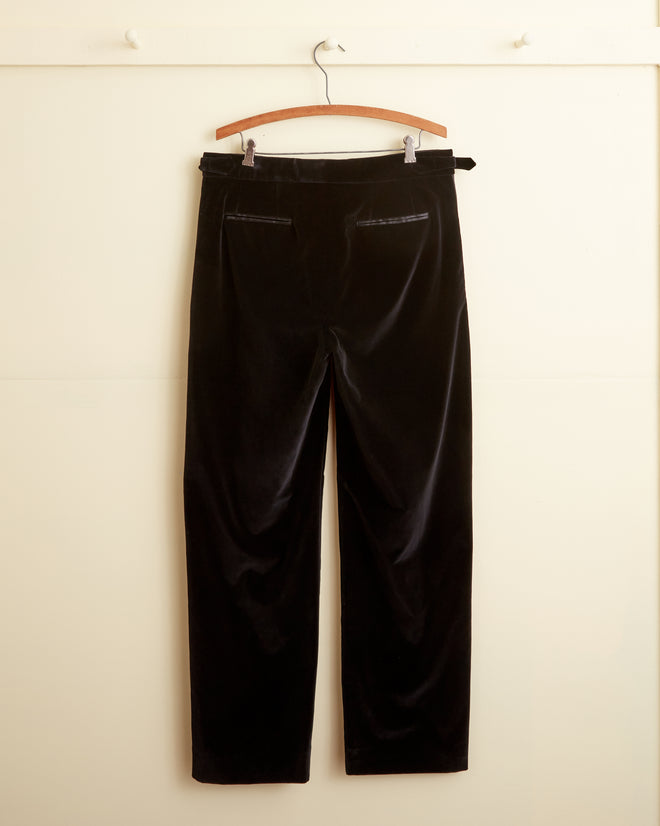 Black Tulip Tuxedo Trousers hanging on a braided hanger against a light-colored wall.