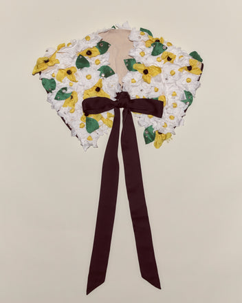 The Blossom Collar features white flowers, green leaves, yellow centers, and a long dark brown ribbon tie—an ideal charming accessory for any Peter Pan costume.
