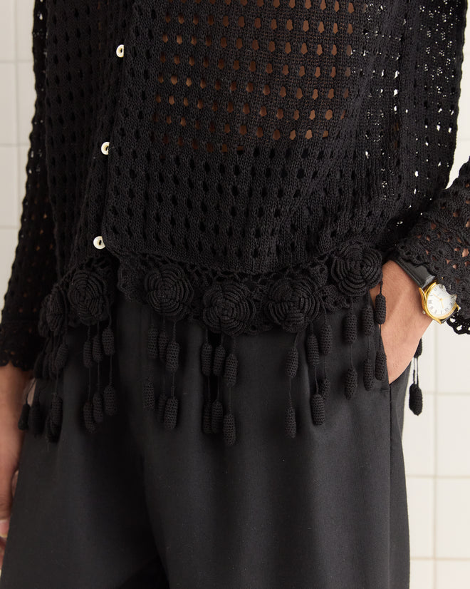 Individual wearing a Blossom Crochet Shirt in black with flower tassels, paired with black pants and a gold watch.