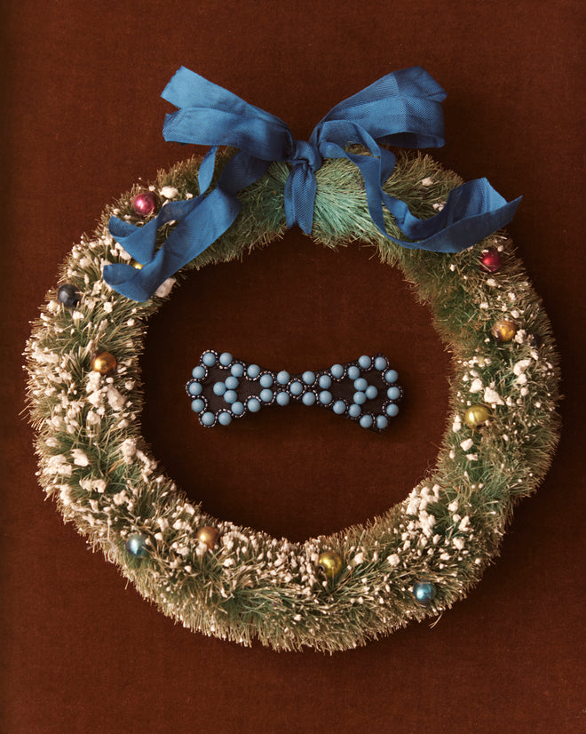 The Blue Bowtie Barrette is adorned with light blue beads and subtle blue studs, arranged in a symmetrical pattern, set against a neutral background.