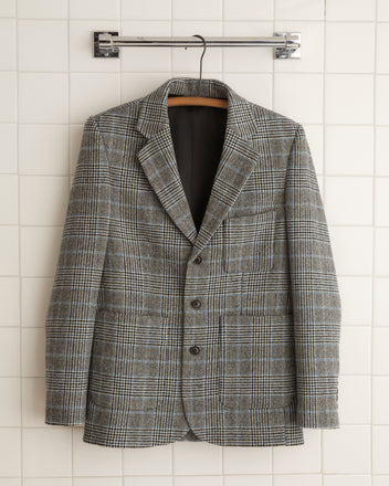 A person wearing the Blue Mountain Suit Jacket - 36 paired with wide-leg trousers made from 1960s suiting fabric stands by a wooden wall in a dimly lit room.