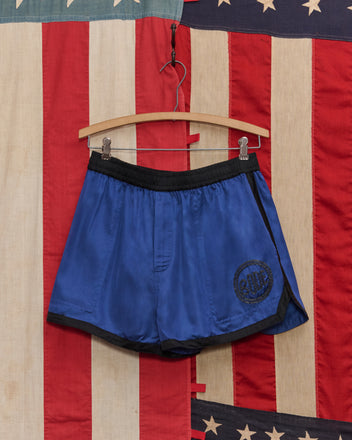 Satin Gym Shorts - Blue/Black hang on a wooden hanger in front of an American flag backdrop.