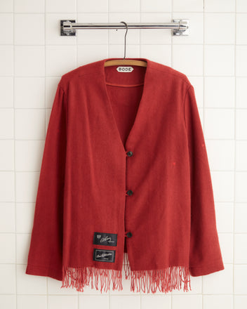 A Blushing Cashmere Jacket - 8, reminiscent of a midcentury throw blanket, hangs stylishly on a hanger against a tiled wall.