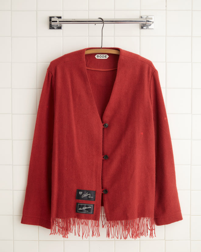 A Blushing Cashmere Jacket - 8, reminiscent of a midcentury throw blanket, hangs stylishly on a hanger against a tiled wall.