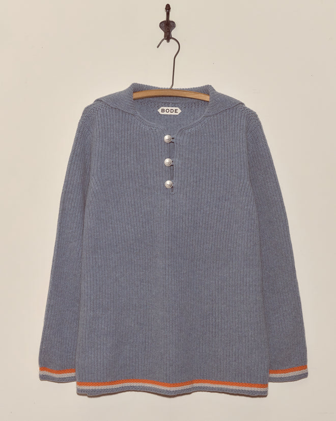 A Boat Deck Pullover—a blue ribbed virgin wool sweater with pirate ship buttons, orange-striped cuffs, and a "BODE" label—hangs on a hook.