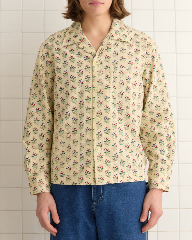 A person in a Boston Flower Long Sleeve Shirt, featuring a charming bouquet motif on yellow, 100% cotton fabric, paired with blue jeans, stands against a tiled background.