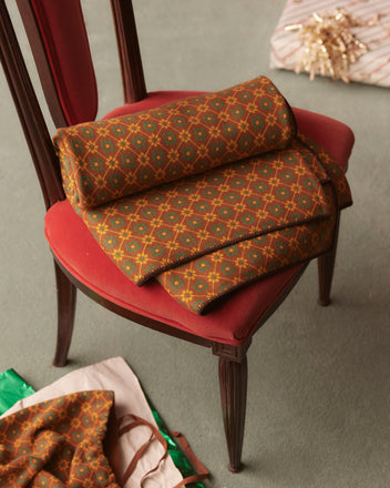 The Floral Jacquard Throw - Brown is draped over a red cushioned chair, with more of the throw spread across the floor.