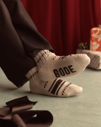 A pair of white Braided Socks, made from merino wool and featuring brown zigzag and stripe patterns with intricate chevron embroidery detailing, laid flat side by side on a light-colored surface.